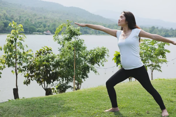 Asiatische schwangere Frau praktiziert Yoga auf grünem Gras in der Öffentlichkeit pa — Stockfoto