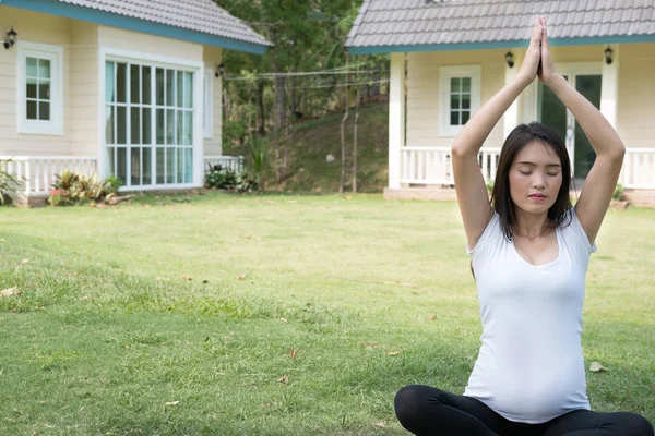 Asiatische schwangere Frau praktiziert Yoga auf grünem Gras vor — Stockfoto