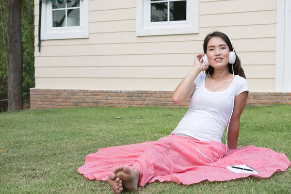 Jovem mulher asiática sentada na grama fresca primavera ouvindo mus — Fotografia de Stock