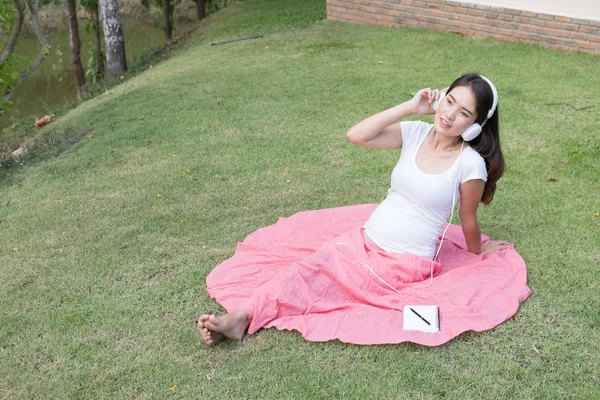 Jeune femme asiatique assis dans l'herbe fraîche de printemps écoute mus — Photo