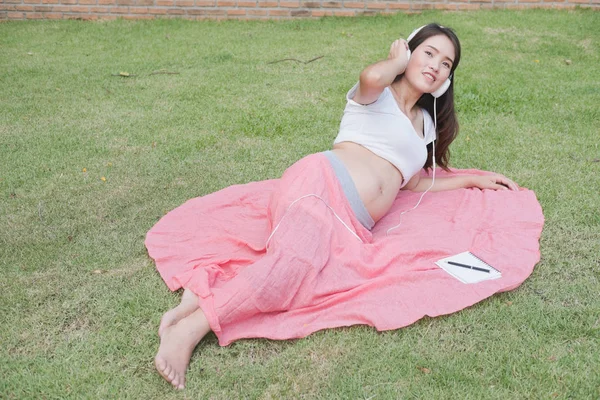 Jeune femme asiatique assis dans l'herbe fraîche de printemps écoute mus — Photo