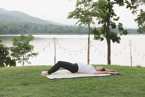 Asiático embarazada mujer practicando yoga en verde hierba en público pa — Foto de Stock