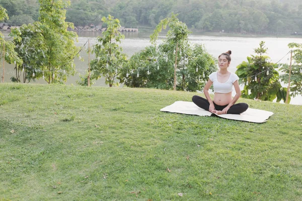 Asiático embarazada mujer practicando yoga en verde hierba en público pa — Foto de Stock