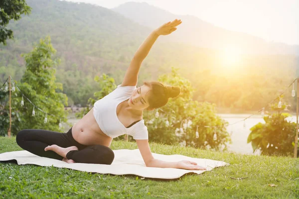 Asiatische schwangere Frau praktiziert Yoga auf grünem Gras in der Öffentlichkeit pa — Stockfoto