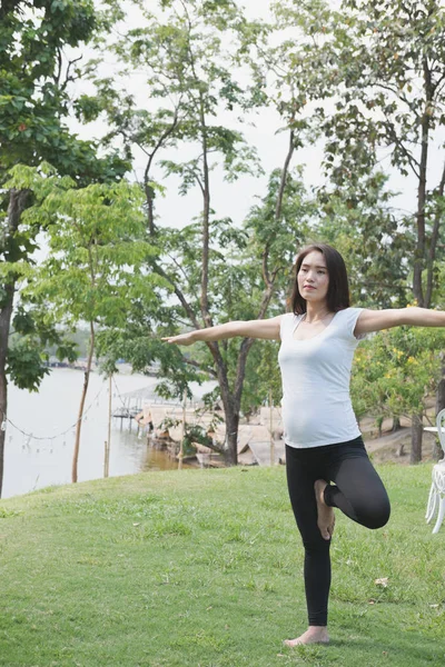 Asiático embarazada mujer practicando yoga en verde hierba en público pa — Foto de Stock