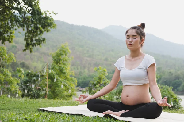 Asiatische schwangere Frau praktiziert Yoga, während sie in Lotus Posi sitzt — Stockfoto