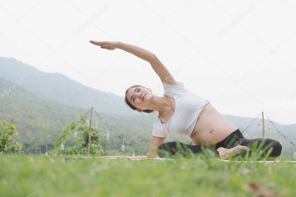 asian pregnant woman practicing yoga on green grass in public pa