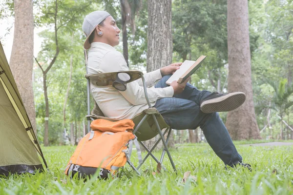 Молодой человек турист сидит на стуле и читает книгу перед — стоковое фото