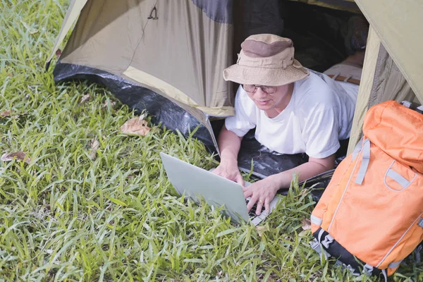 Молодой человек турист лежа и используя ноутбук в палатке в кемпинге — стоковое фото