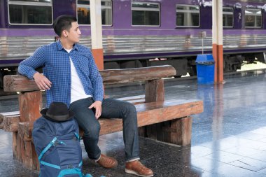 sırt çantası platformda tren istasyonunda oturan Asya adam. ba