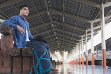 sırt çantası platformda tren istasyonunda oturan Asya adam. ba