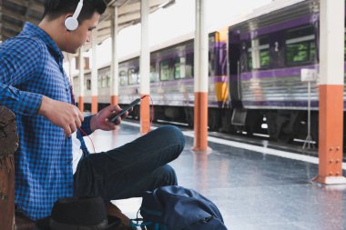 sırt çantası platformda tren istasyonunda oturan Asya adam. ba