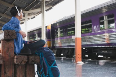 sırt çantası platformda tren istasyonunda oturan Asya adam. ba