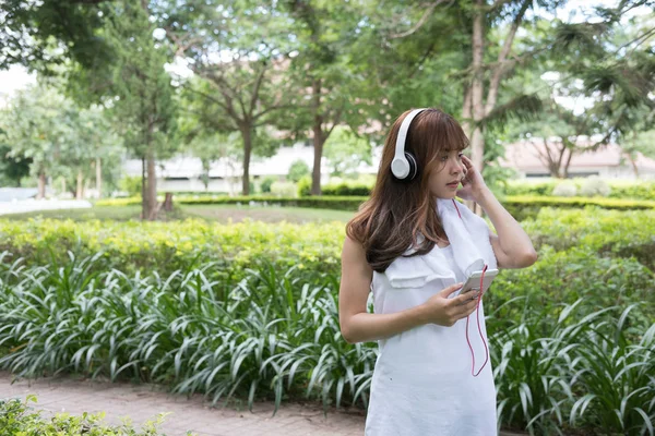 Mulher asiática com fones de ouvido. jovem fêmea segurando inteligente móvel — Fotografia de Stock