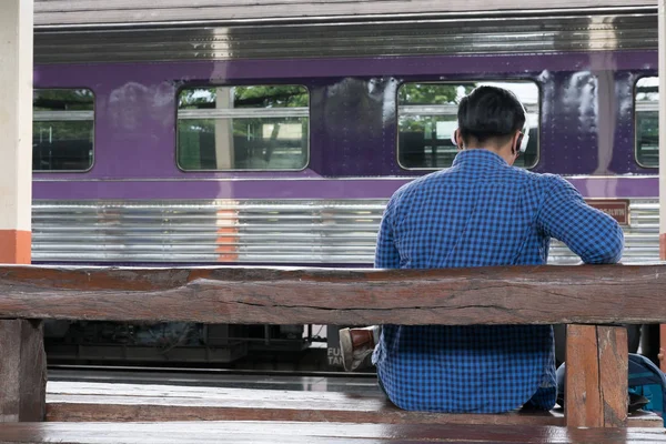 Uomo asiatico con zaino seduto sulla piattaforma alla stazione ferroviaria. ba — Foto Stock