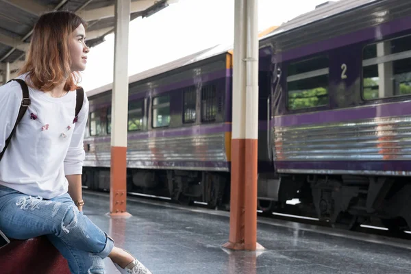 Ázsiai nő ül a platform vasútállomáson bőrönddel. — Stock Fotó