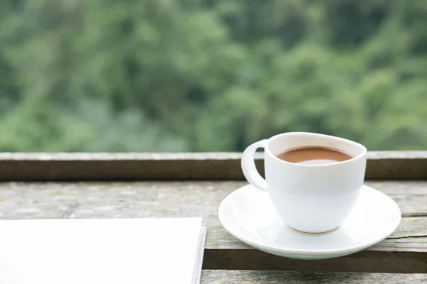 Heißer Kaffee in weißer Tasse auf Holztisch mit grünem Naturhintergrund — Stockfoto