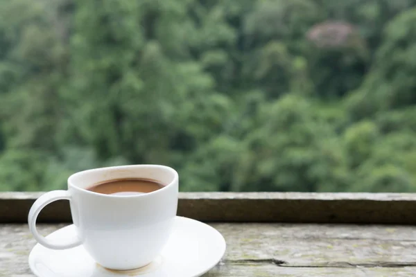 Heißer Kaffee in weißer Tasse auf Holztisch mit grünem Naturhintergrund — Stockfoto