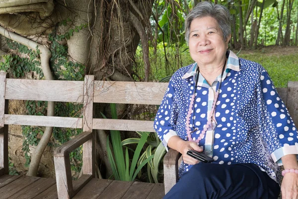 채널에 앉아있는 동안 모바일 스마트 폰 들고 아시아 노인 여성 — 스톡 사진