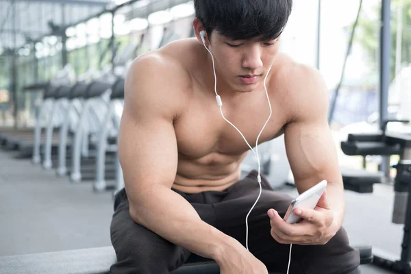 young man use mobile phone in fitness center. male athlete liste