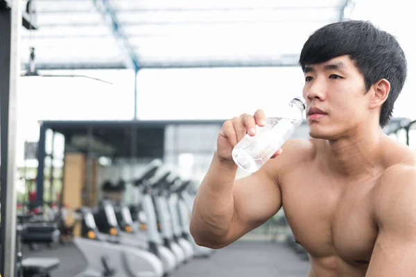 young man drinking water in fitness center. male athlete feeling