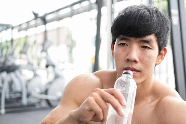 young man drinking water in fitness center. male athlete feeling