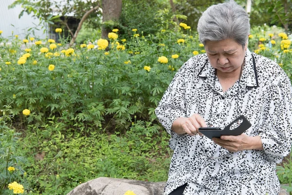 elder woman holding mobile phone while sitting on bench in garde