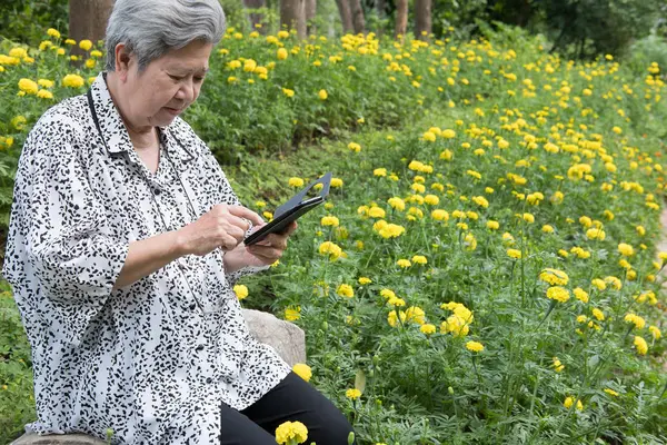 Anciana sosteniendo el teléfono móvil mientras está sentada en el banco en garde — Foto de Stock