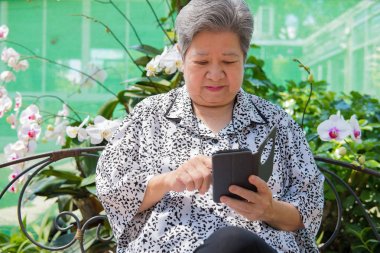 garde bankta otururken cep telefonu tutan yaşlı kadın