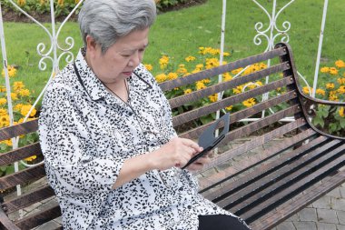 garde bankta otururken cep telefonu tutan yaşlı kadın