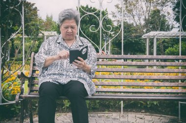 garde bankta otururken cep telefonu tutan yaşlı kadın