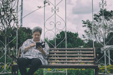 garde bankta otururken cep telefonu tutan yaşlı kadın