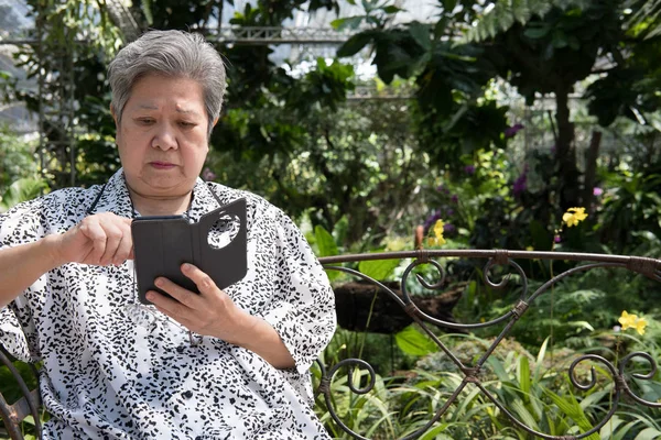 Anciana sosteniendo el teléfono móvil mientras está sentada en el banco en garde — Foto de Stock