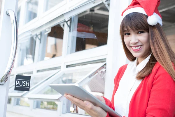 Mulher usar chapéu de Papai Noel segurando tablet em sua loja. asiático feminino nós — Fotografia de Stock