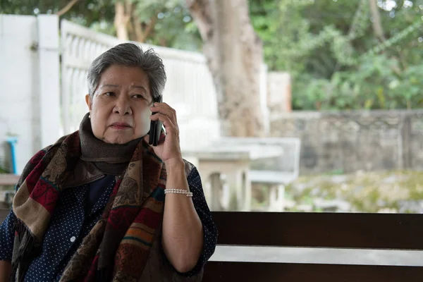 Elder woman talk on mobile phone while sitting on bench in garde — Stock Photo, Image