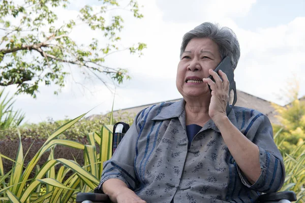 elder woman in wheelchair talk on mobile phone in garden. elderl
