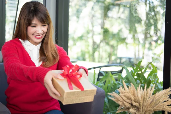 Femme portant un pull rouge tenant boîte cadeau à la maison. fille avec pr — Photo