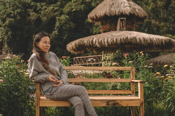 Jonge vrouw zitten op houten bankje in het park. meisje ontspannen in de tuin. — Stockfoto