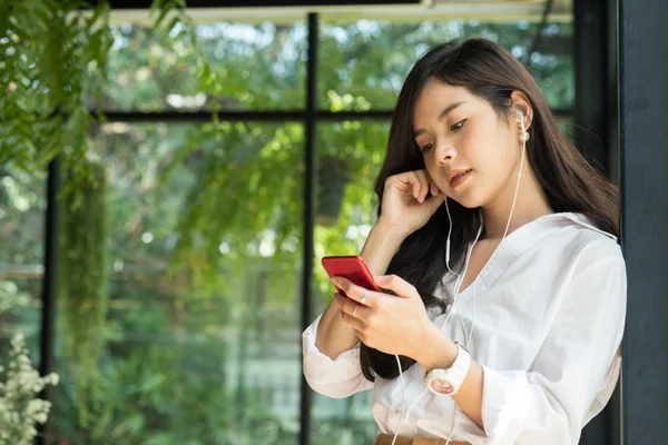 Женщина держит смартфон и слушает музыку с наушниками — стоковое фото