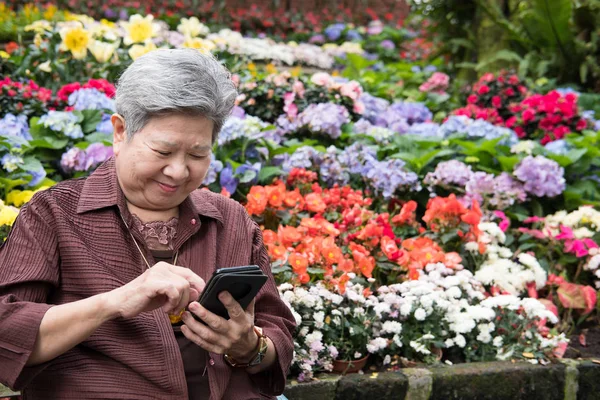 elder woman holding mobile phone in garden. elderly female texti