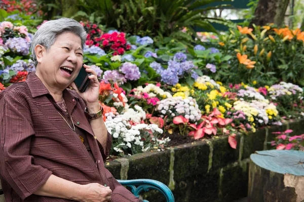 老妇人在花园里用手机说话。老年女性发言 — 图库照片