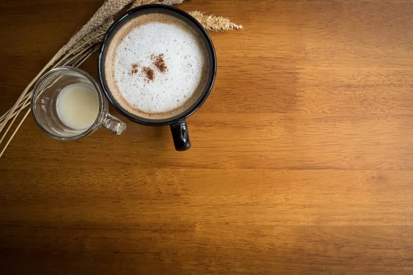 Cafea fierbinte cappuccino cu pulbere de scorțișoară în ceașcă neagră pe lemn — Fotografie, imagine de stoc