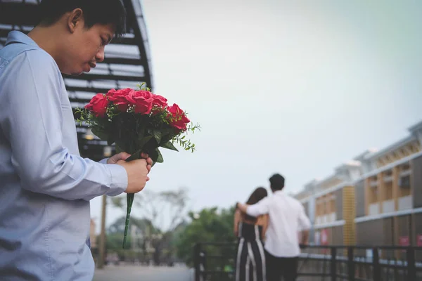 heartbroken man holding bouquet of red roses feeling sad while s