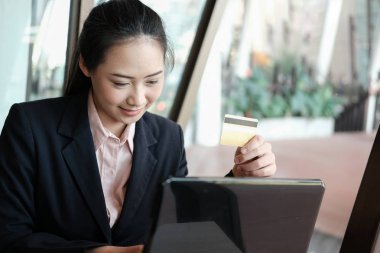 bir kredi kartı tutan ve online shoppi için bilgisayarı kullanan kadın