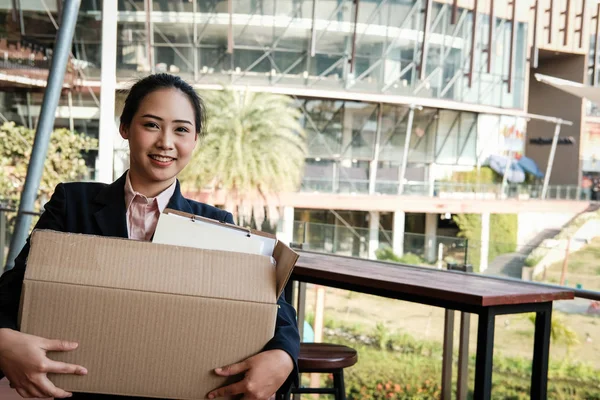 happy woman resigning her job & holding cardboard box containing