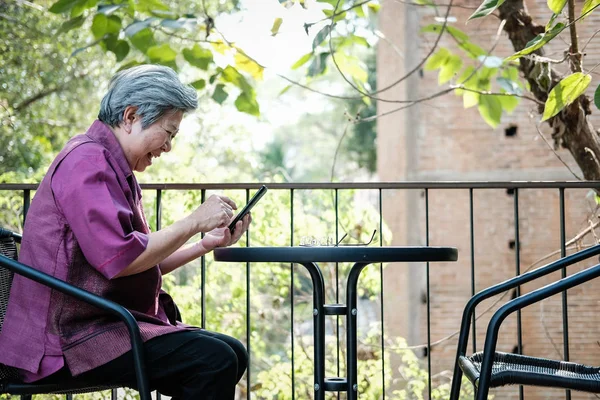 Anciana sosteniendo teléfono móvil en la terraza. texto femenino de edad avanzada — Foto de Stock