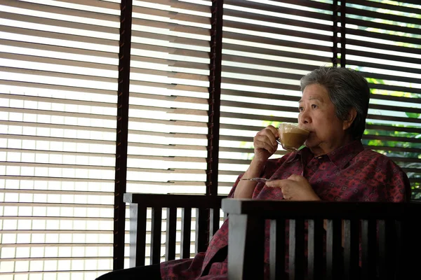 Азіатська літня жінка сидить і відпочиває в кафе з чашкою шапки — стокове фото