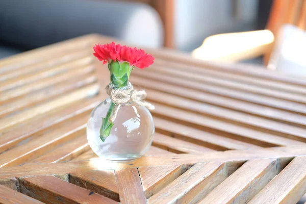 Červená květina ve skleněné láhvi váza na dřevěném stole — Stock fotografie