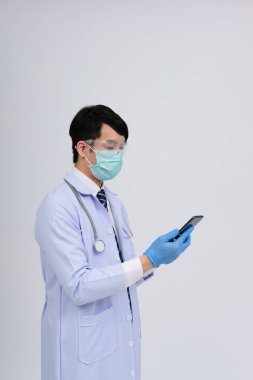Doktor doktor doktor, maske takıyor ve beyaz arka planda akıllı telefon ve steteskop var. Tıbbi profesyonel tıp sağlık hizmeti kavramı