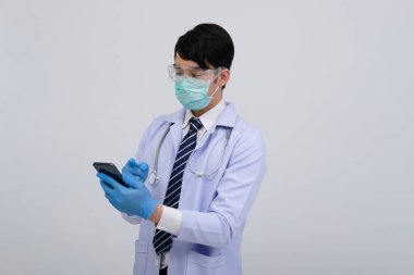 Doktor doktor doktor, maske takıyor ve beyaz arka planda akıllı telefon ve steteskop var. Tıbbi profesyonel tıp sağlık hizmeti kavramı